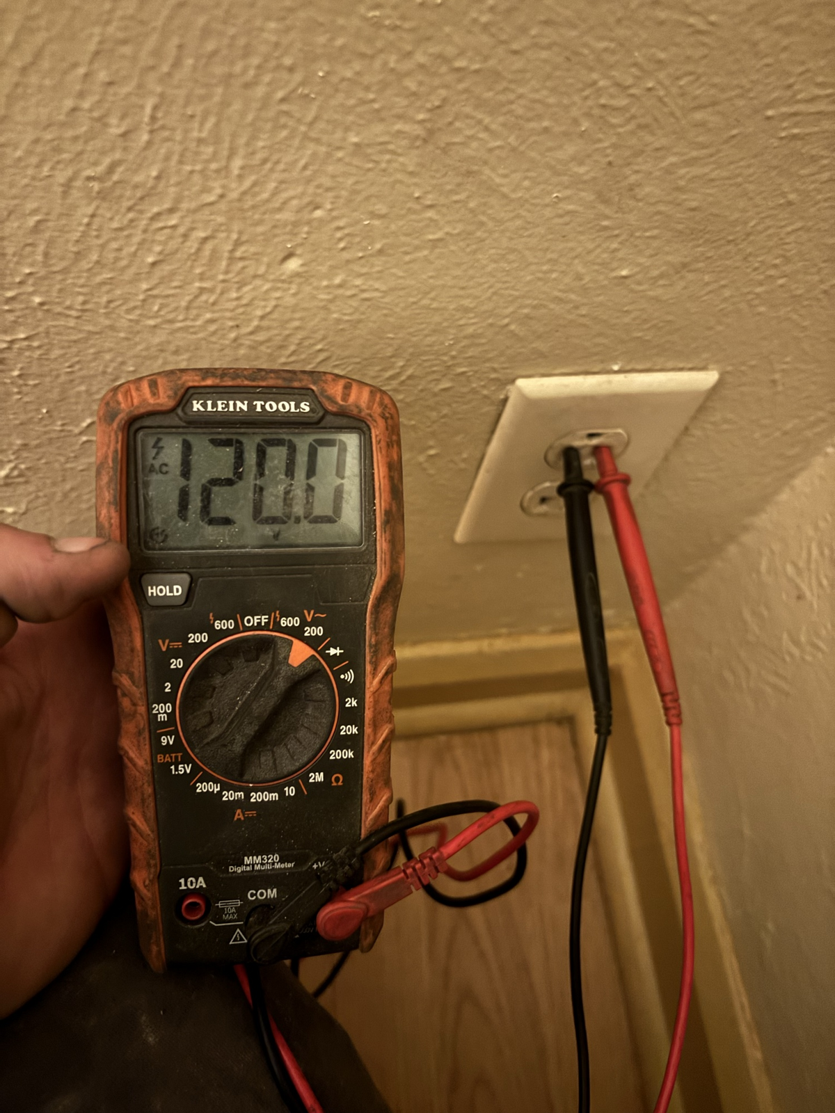 Electrician using a multimeter to test voltage at a wall outlet, reading 120V AC